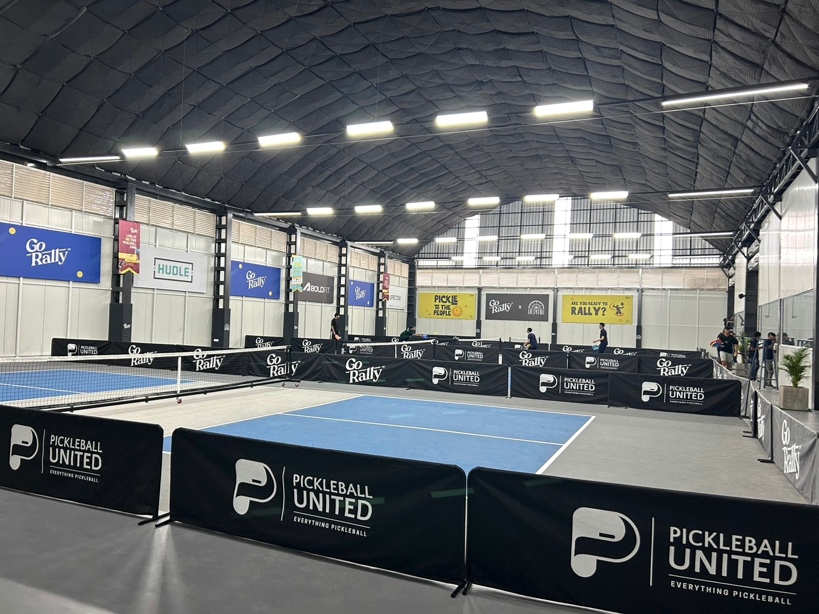 Indoor sports facility with marked playing courts beneath a large-span roof structure.