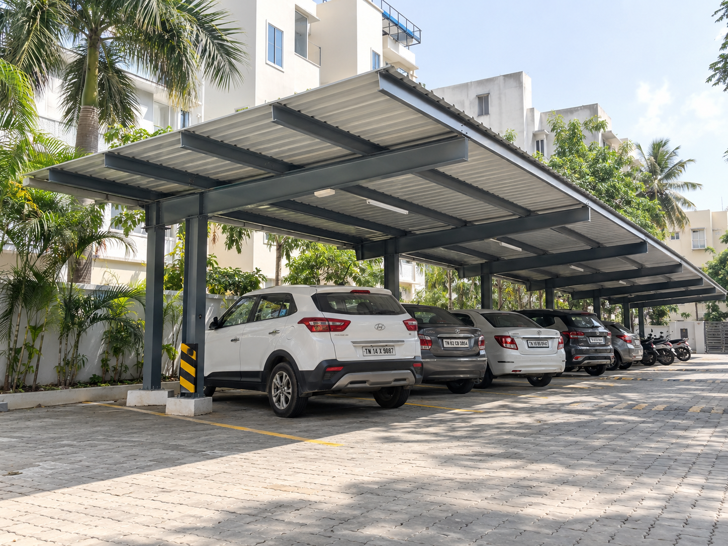 Covered parking shed with steel framework, metal roofing and vehicles parked beneath the shelter.